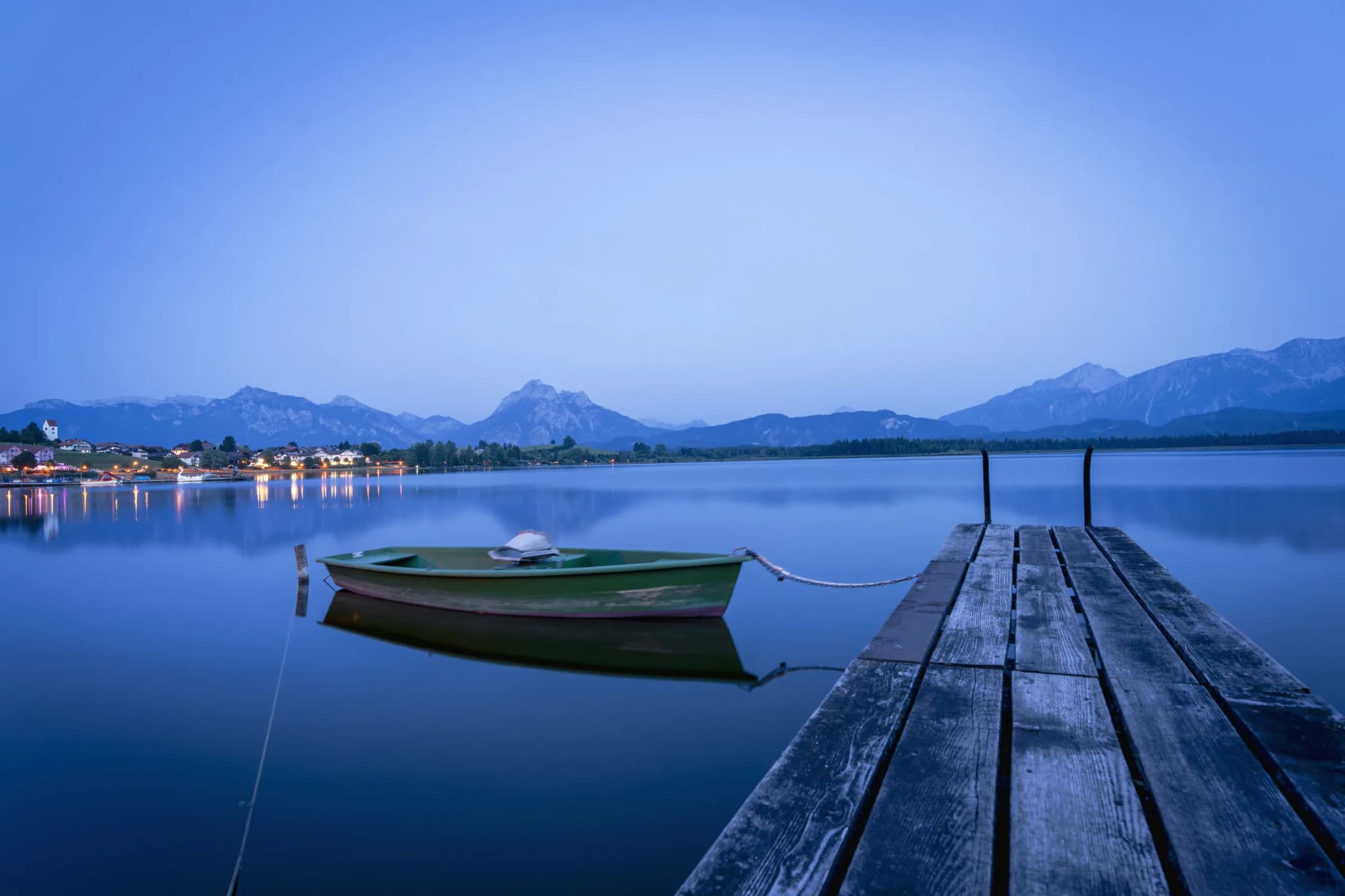 A small boat beside a quiet dock with mountains across the water