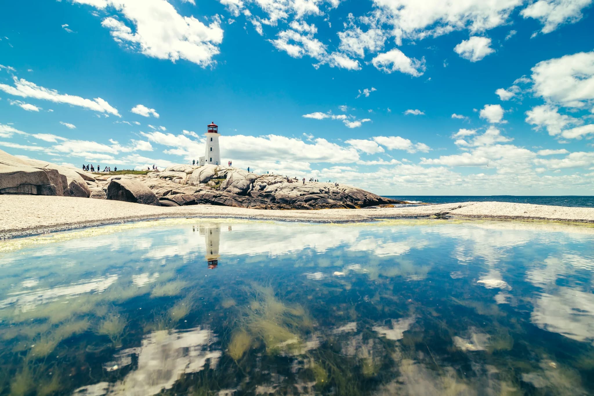 A lighthouse standing above a rocky cove and calm reflective water